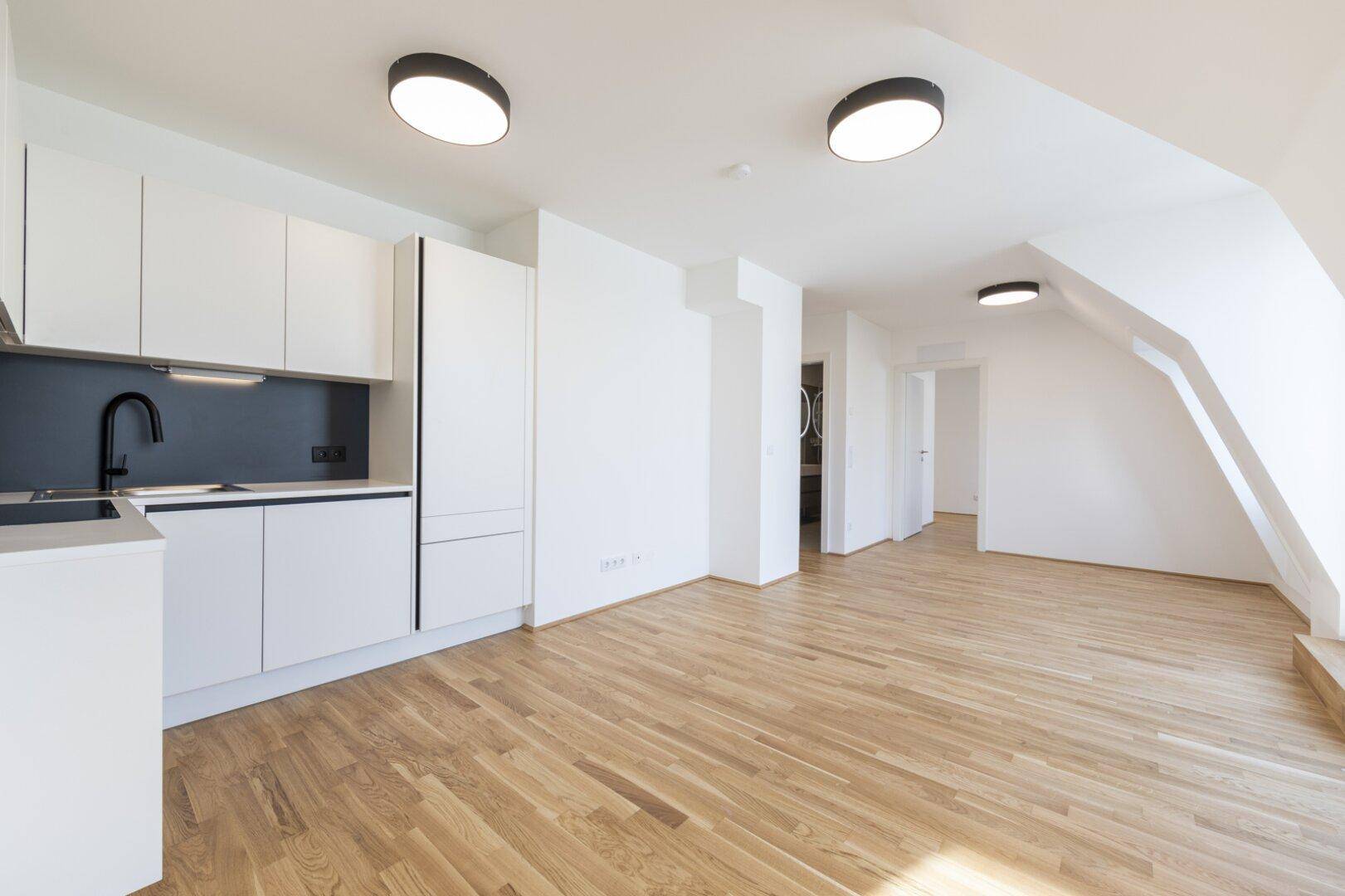 Moderner Wohnbereich mit integrierter Küchenzeile, Parkettboden und viel Tageslicht im Dachgeschoss.