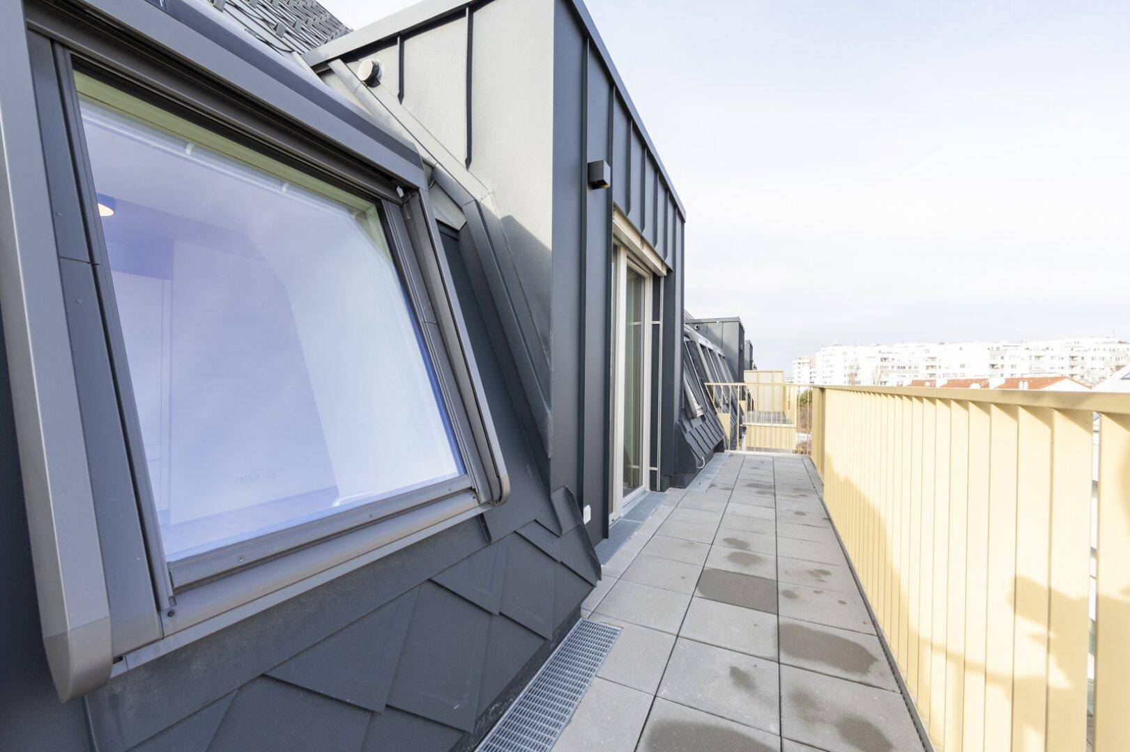 Lange Dachterrasse mit Fliesenboden und gelbem Geländer, bietet einen weiten Blick über die Stadt.