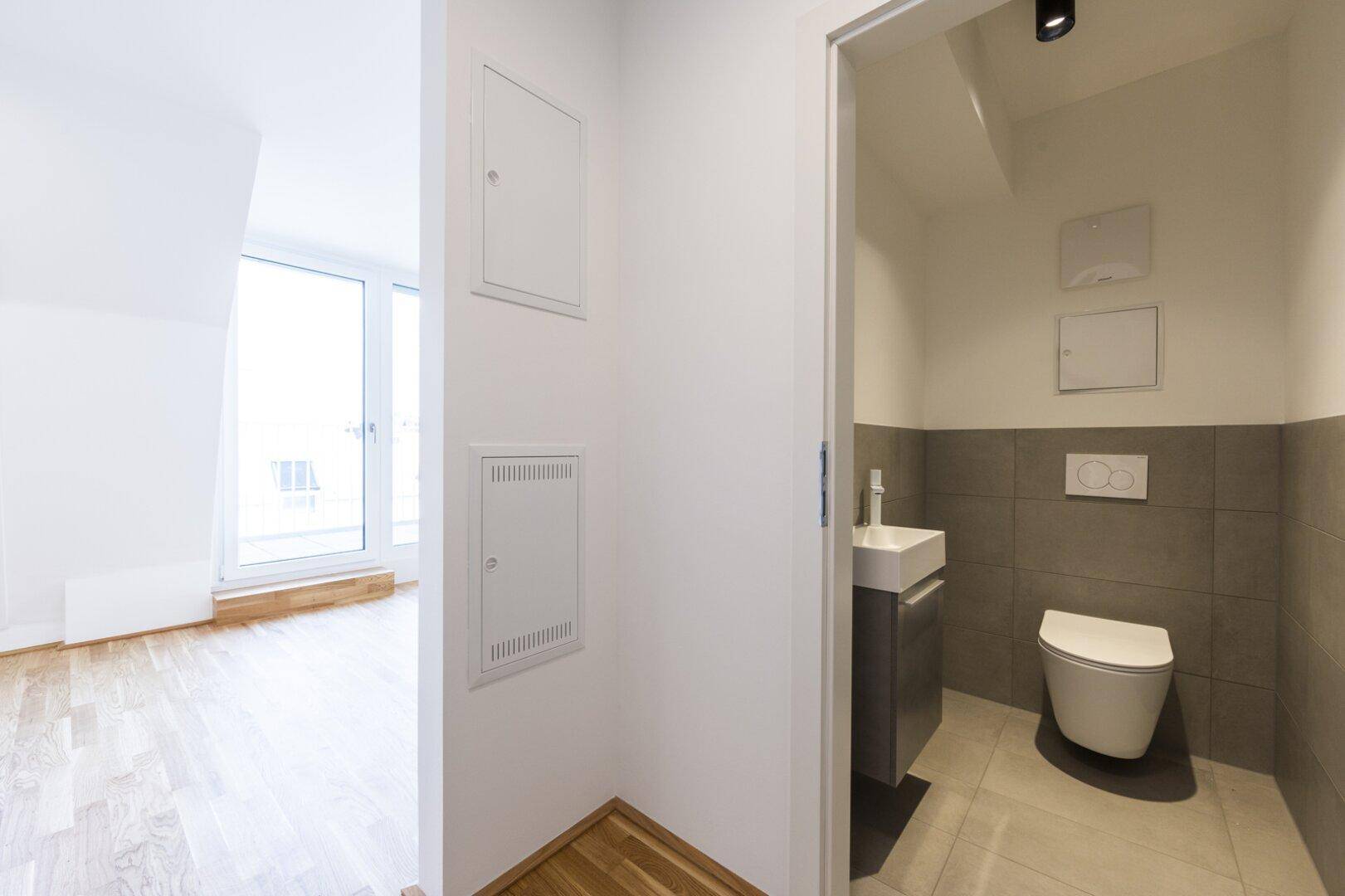 Modernes Gäste-WC mit Wand-WC, Waschbecken und grauen Fliesen im unteren Wandbereich.