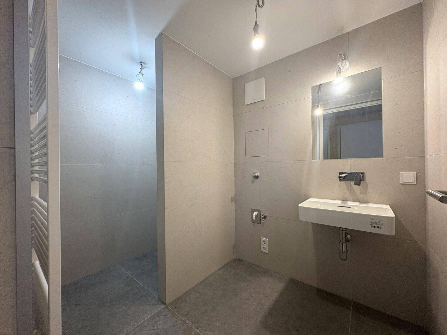 Modernes Badezimmer mit beigefarbenen Fliesen, schwebendem Waschbecken und Handtuchheizkörper.