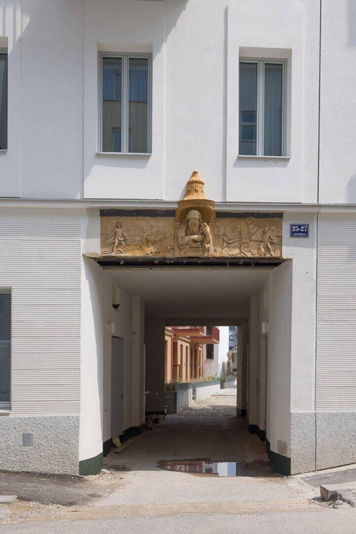 Historischer Durchgang mit Reliefverzierung und Blick auf den Innenhof eines Wohnkomplexes.