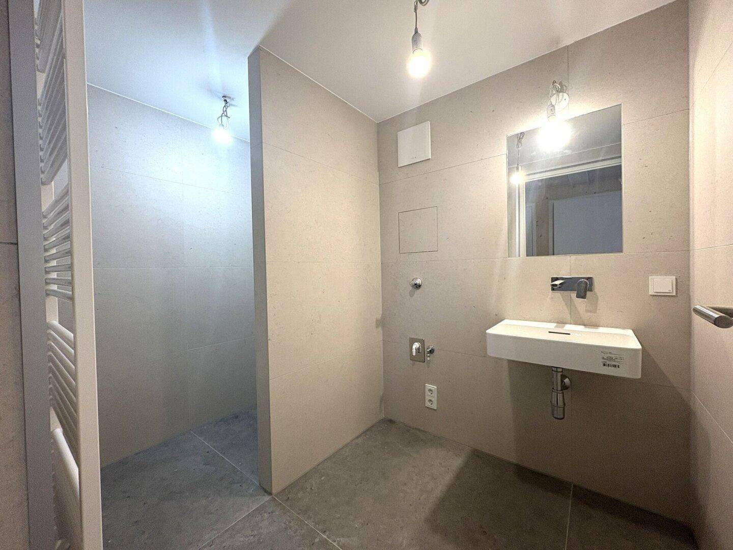 Modernes Badezimmer mit beigefarbenen Fliesen, schwebendem Waschbecken und Handtuchheizkörper.