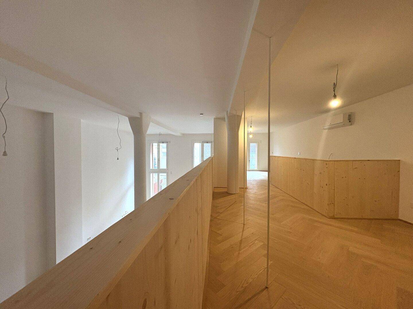 Heller Wohnbereich mit Fischgrätparkett, hohen Decken und einer Holzbrüstung.