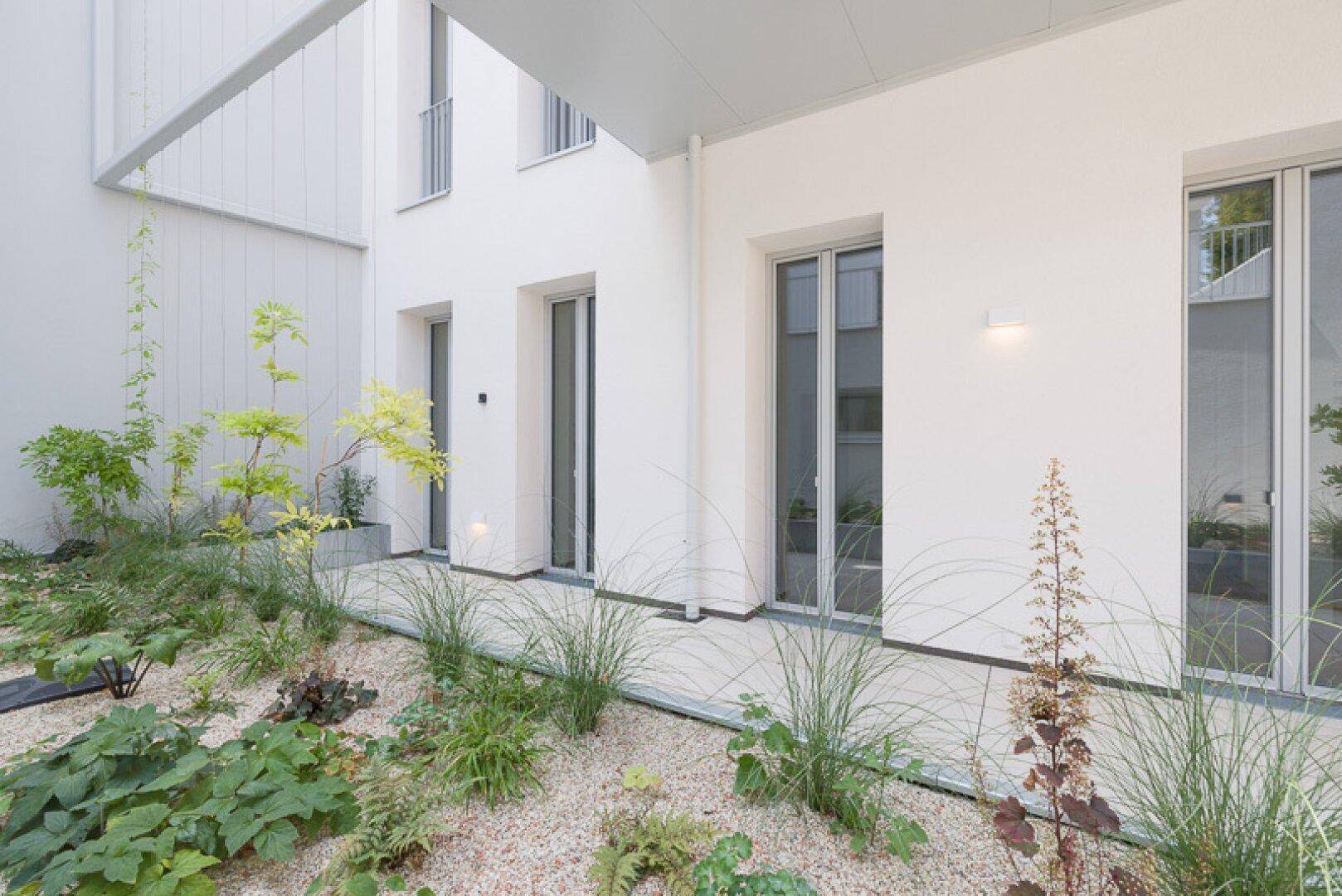 Mediterran gestalteter Gartenbereich im Innenhof mit Kies und verschiedenen Pflanzen.