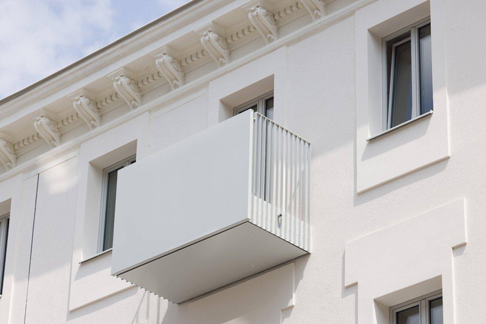 Moderner weißer Balkon an einer hellen Fassade mit dekorativem Gesims.