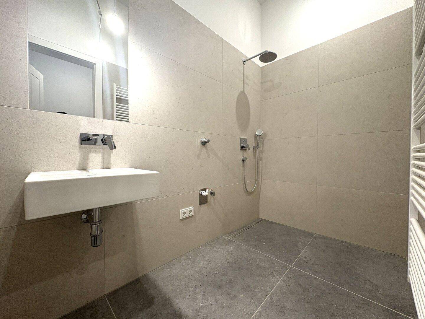 Modernes Badezimmer mit großformatigen Fliesen, Dusche und wandhängendem Waschbecken.