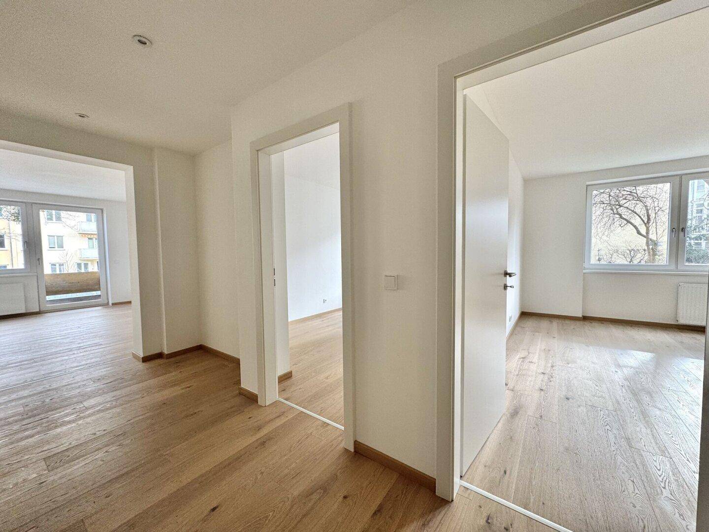 Heller Flur mit Holzboden, der zu verschiedenen Zimmern und einem Balkon führt.