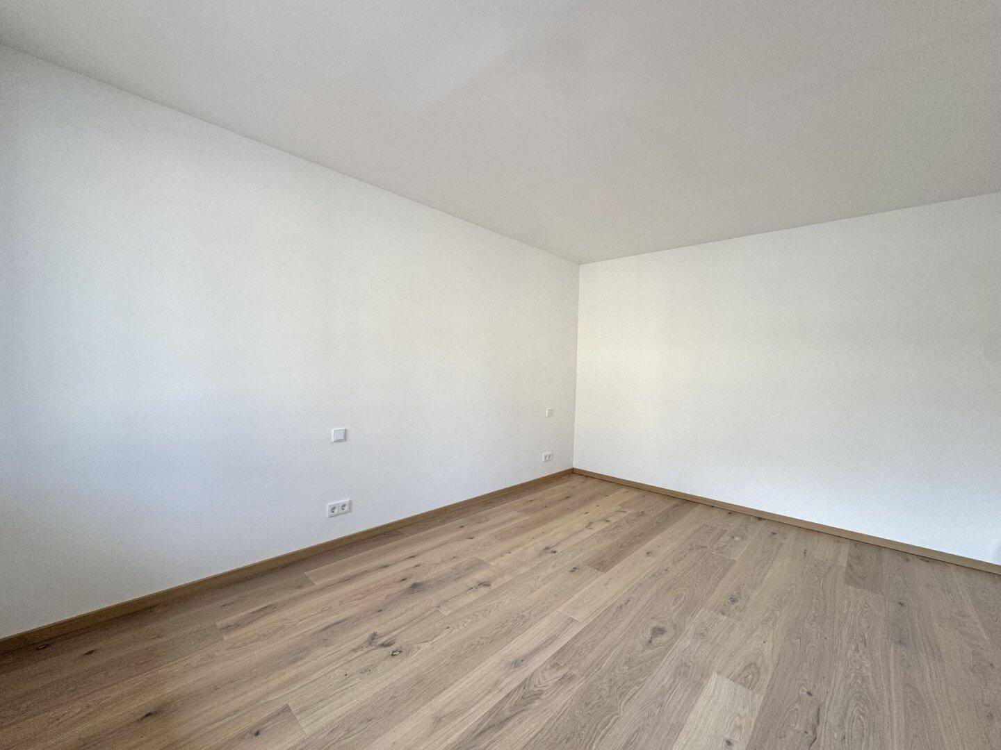 Leeres Zimmer mit hellem Parkettboden und weißen Wänden, ideal als Schlafzimmer.