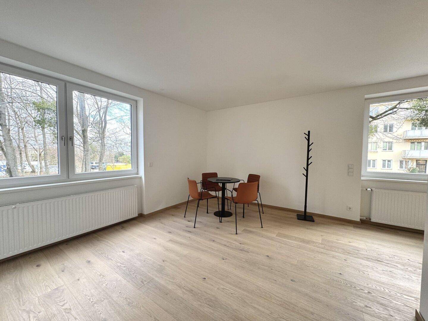 Heller Wohnbereich mit Parkettboden, Essplatz und zwei großen Fenstern für viel Licht.
