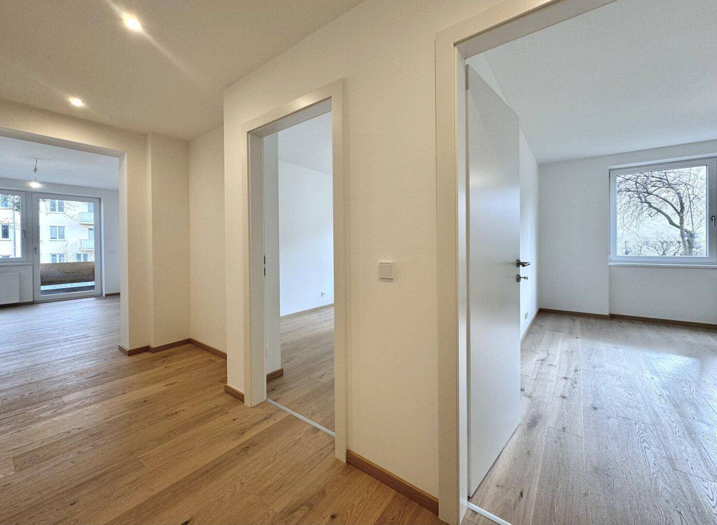 Geräumiger Flur mit Holzboden und offenen Türen, die den Blick in angrenzende Räume freigeben.
