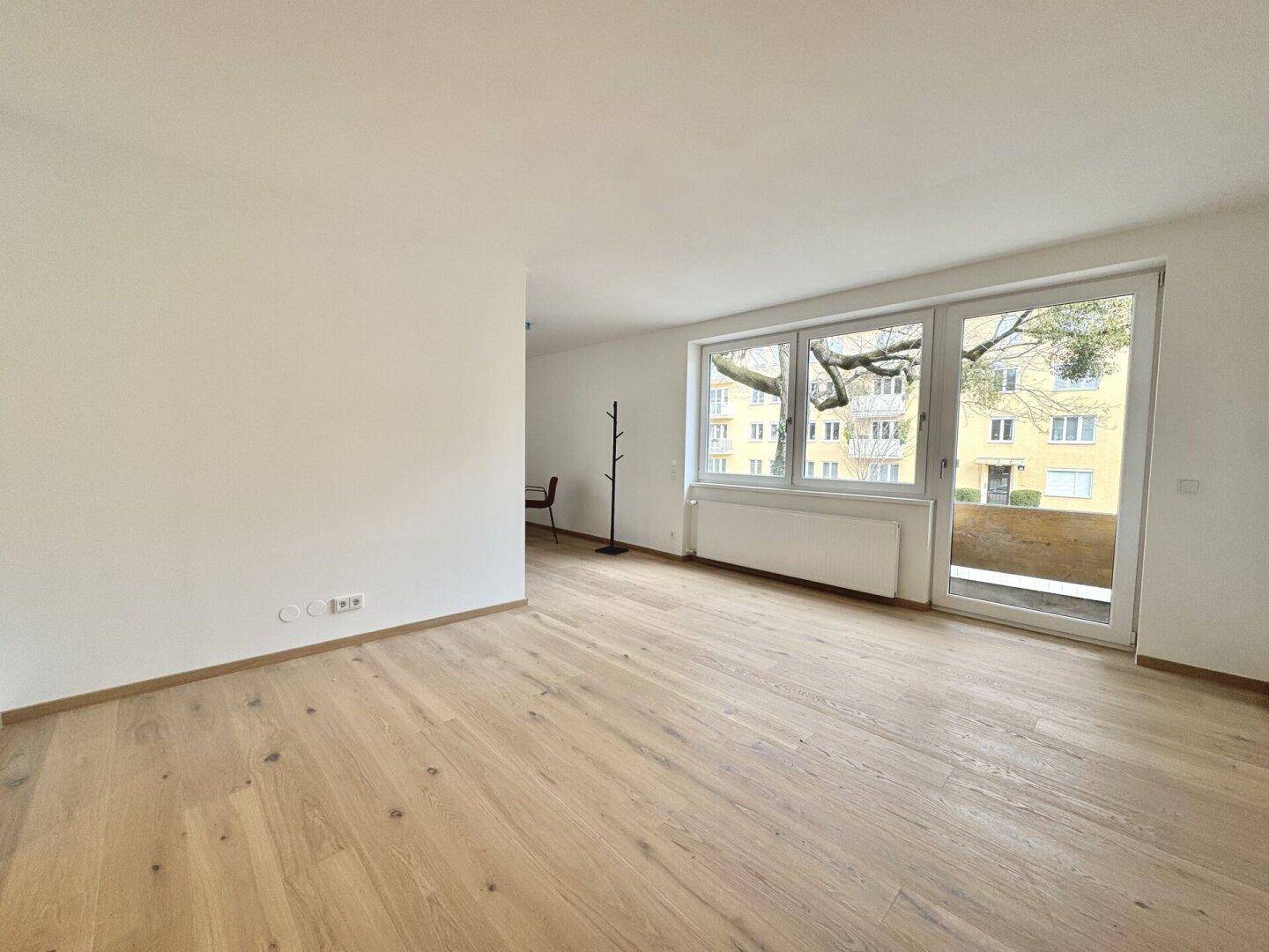 Geräumiges Wohnzimmer mit Holzboden und großem Fenster mit Zugang zum Außenbereich.