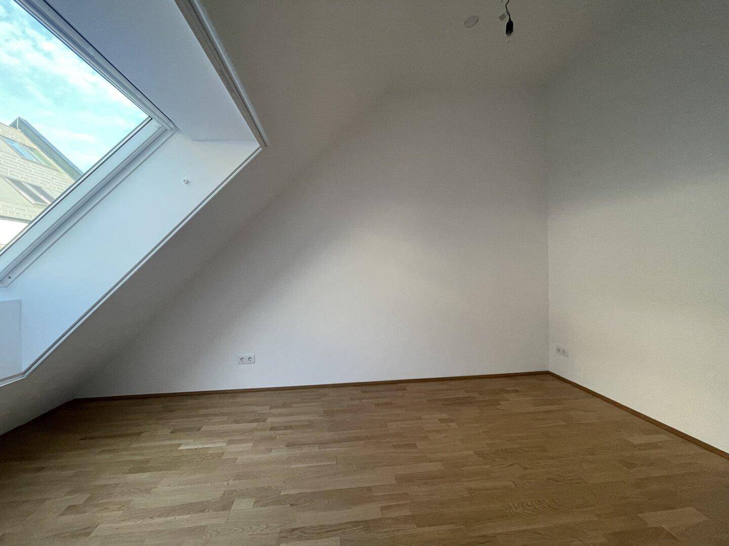 Helles Schlafzimmer im Dachgeschoss mit Holzboden und großem Dachfenster.