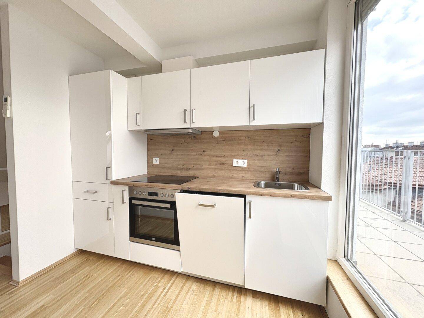 Moderne Küchenzeile mit weißen Schränken, Holzarbeitsplatte und direktem Zugang zur Terrasse.