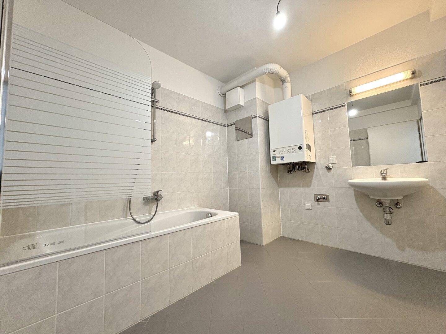 Funktionales Badezimmer mit Badewanne, Duschfunktion, Waschbecken und Gastherme an der Wand.