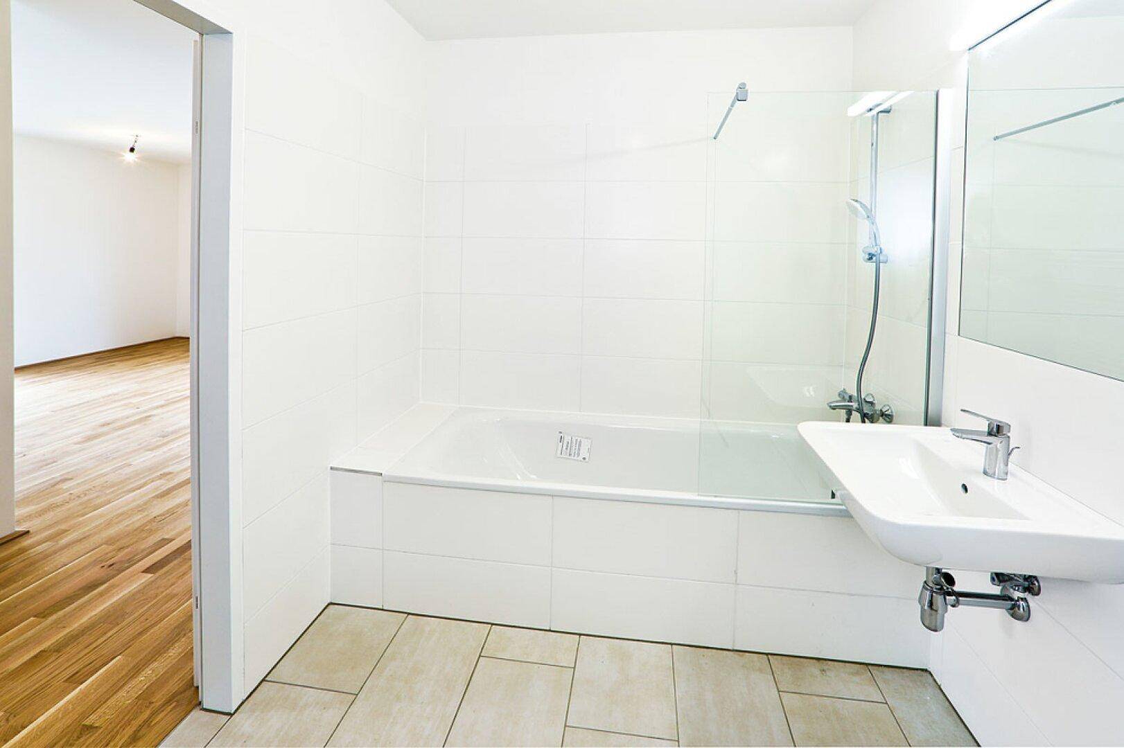 Modernes Badezimmer mit Badewanne, Dusche und Waschbecken, hell gefliest.
