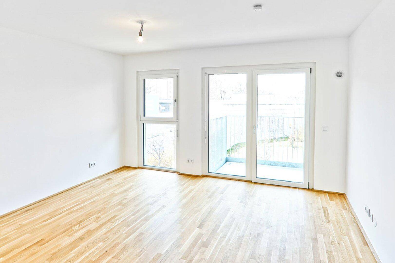 Helles Wohnzimmer mit Parkettboden und Schiebetür zu einem kleinen Balkon.