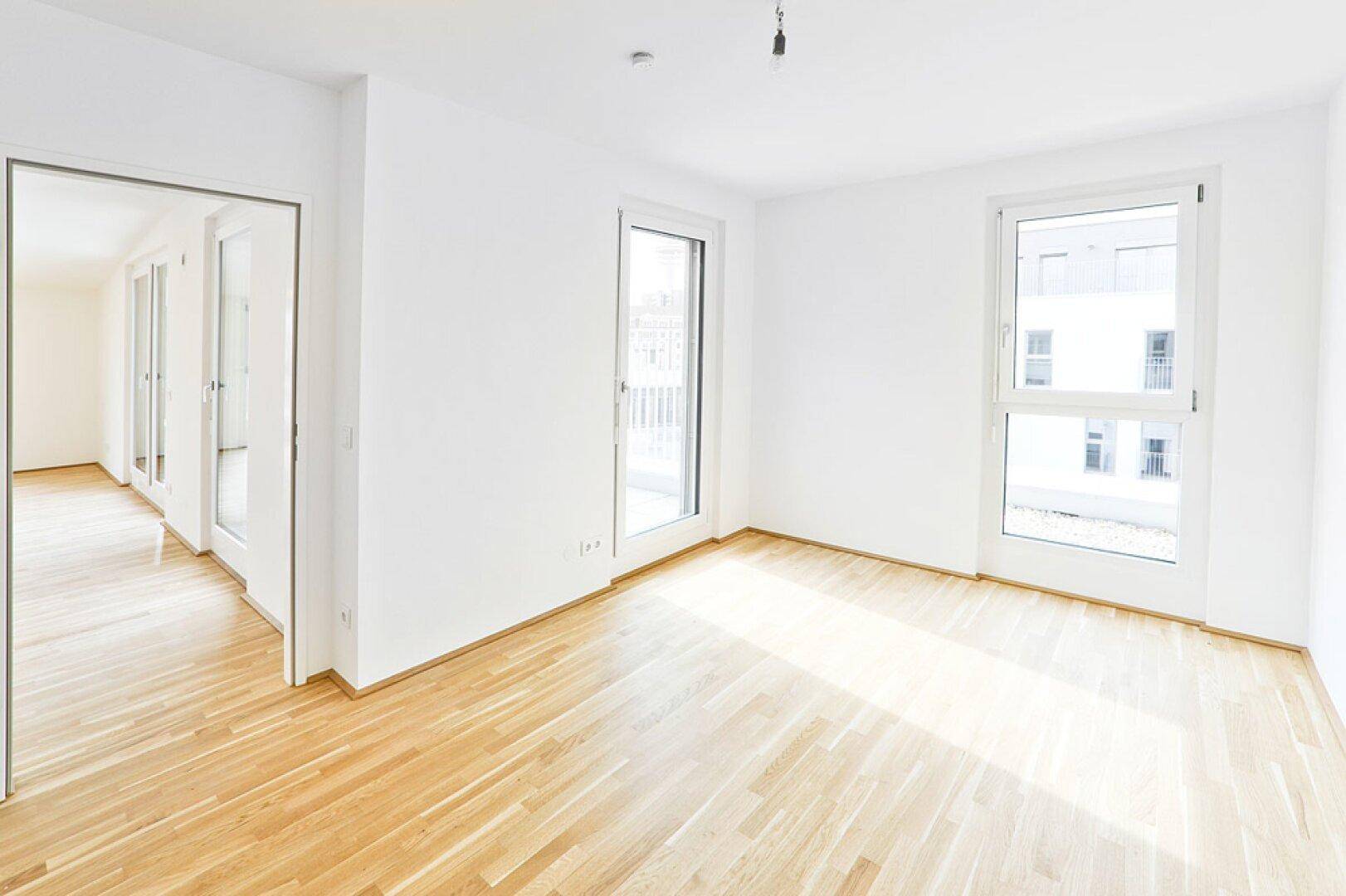 Geräumiges, helles Wohnzimmer mit Parkettboden und Zugang zu einem Balkon.