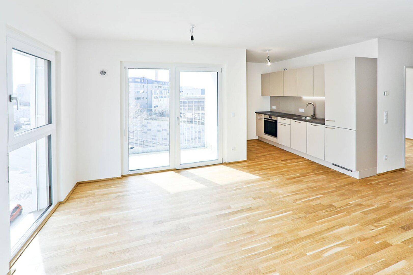 Heller Wohnbereich mit integrierter Küchenzeile und Zugang zum Balkon.