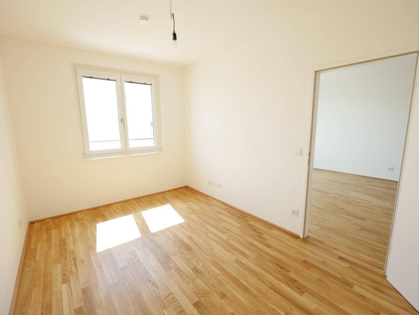 Helles Schlafzimmer mit Parkettboden und einem Fenster, das viel Tageslicht hereinlässt.