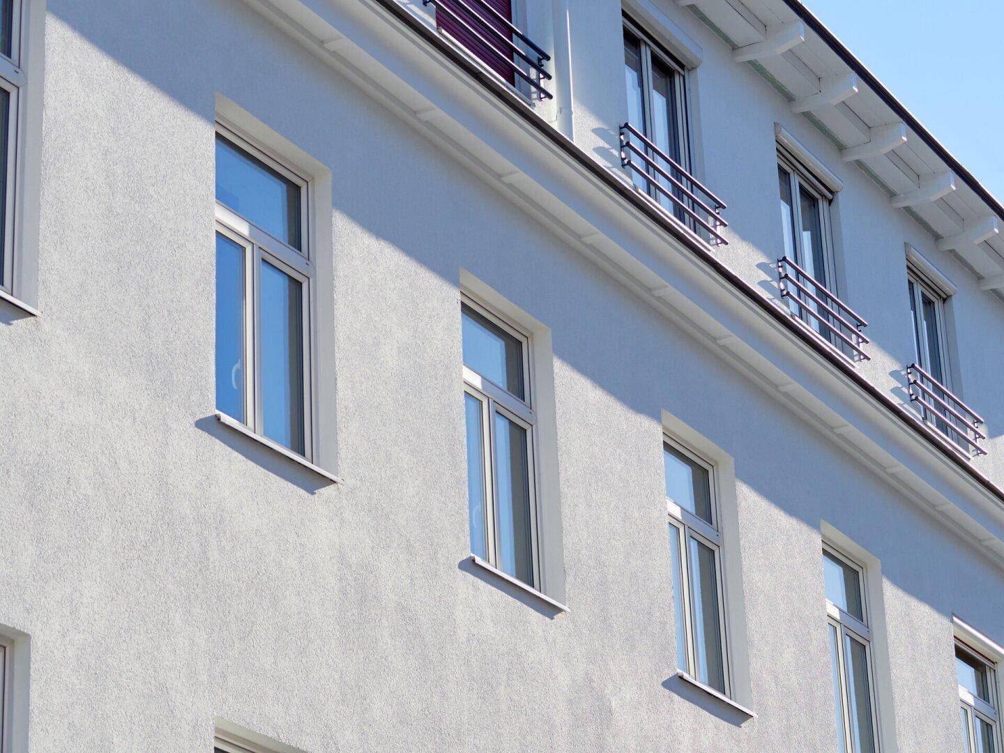 Reihe von Fenstern an der weißen Fassade des Gebäudes, die das Sonnenlicht reflektieren.