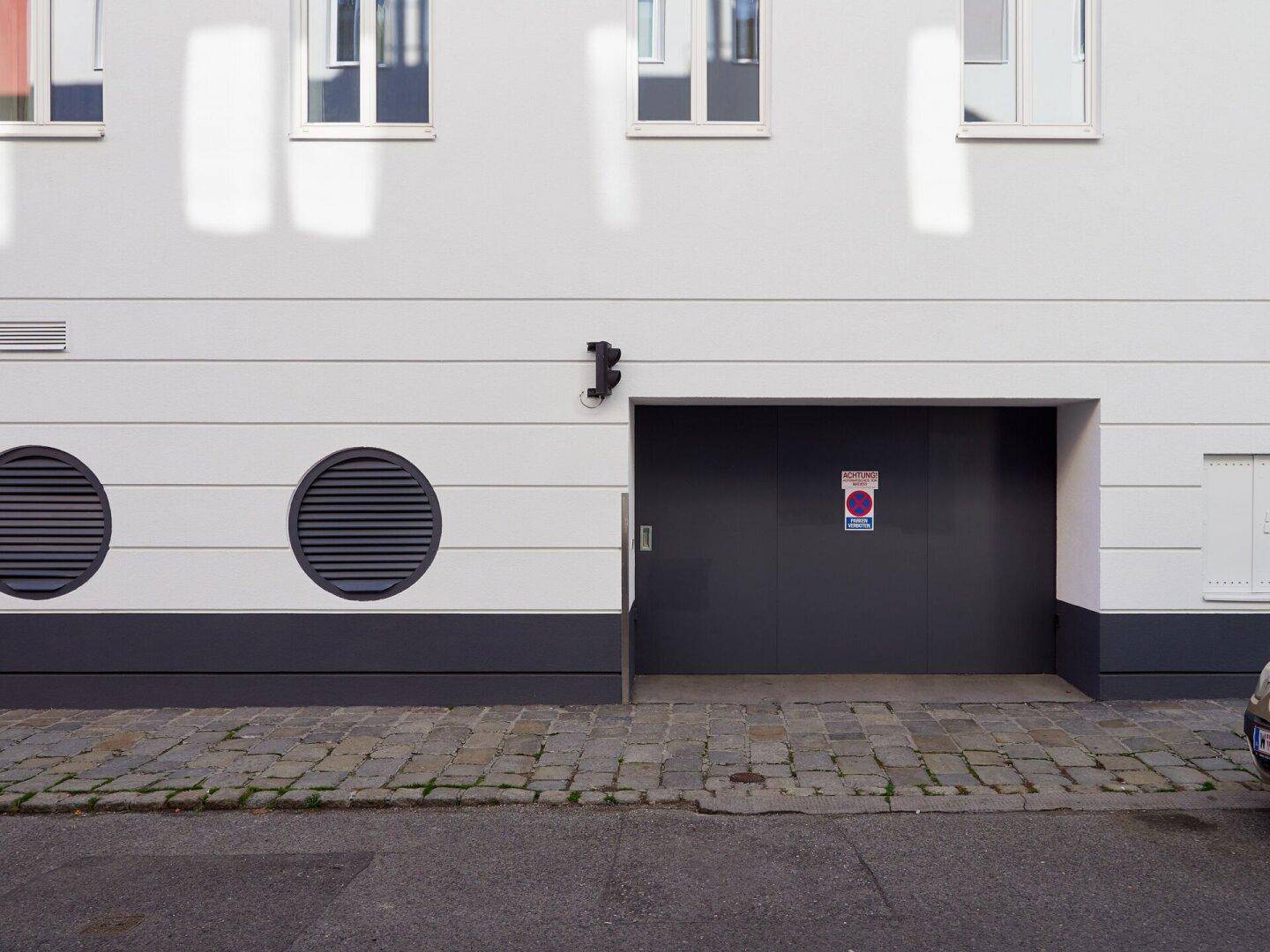 Eingangsbereich und Garagentor des Gebäudes mit runden Lüftungsöffnungen an der Fassade.