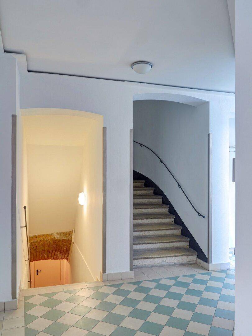 Helles Treppenhaus mit gemustertem Fliesenboden und geschwungener Treppe.