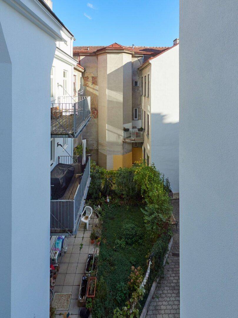 Blick von oben auf einen begrünten Innenhof mit Terrasse und Balkonen der umliegenden Gebäude.