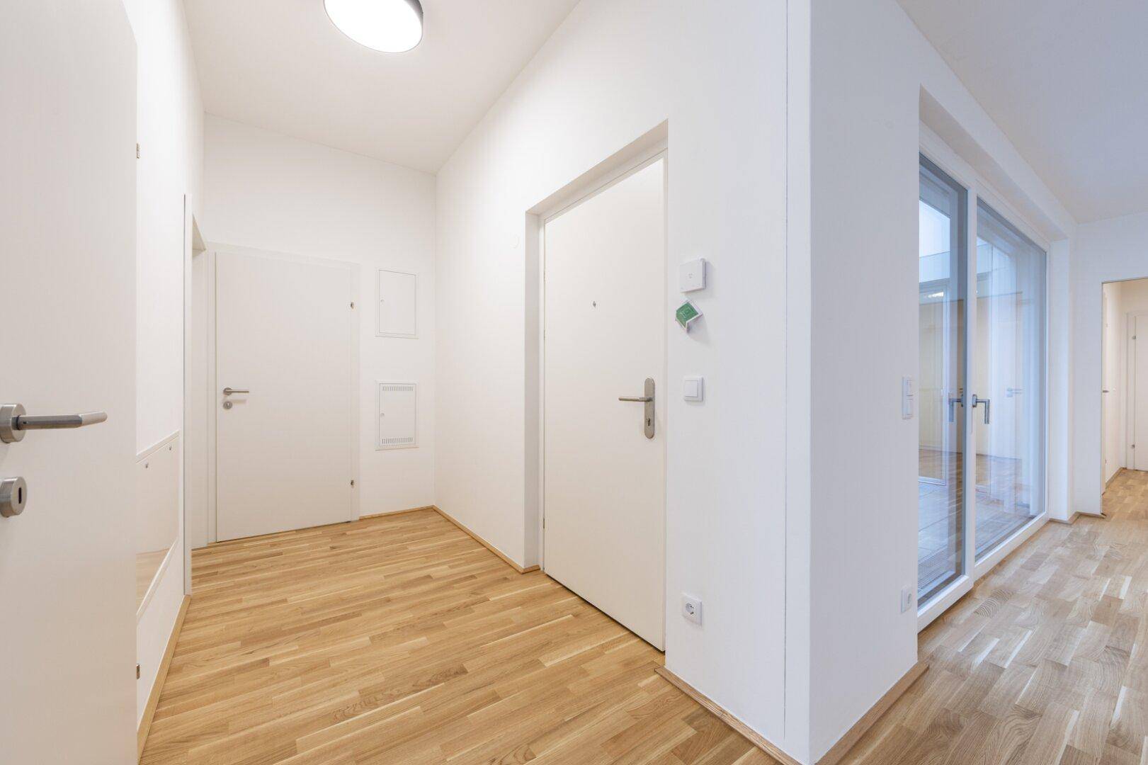 Moderner Flur mit Holzboden, weiß gestrichenen Wänden und einer großen Glaswand, die viel Licht spendet.