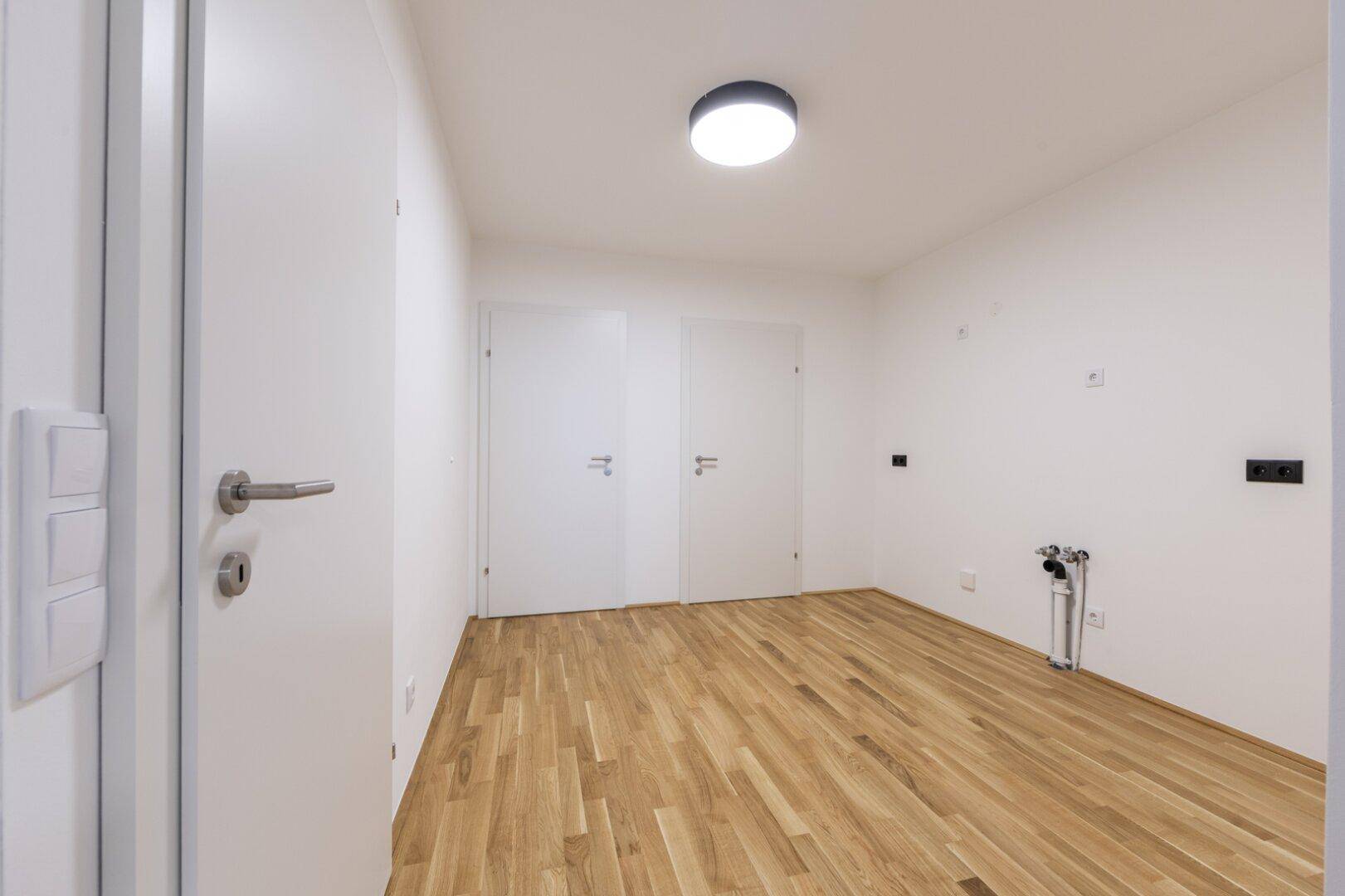 Leeres Zimmer mit Parkettboden, weißen Wänden und Anschlüssen, vielseitig nutzbar als Schlaf- oder Arbeitszimmer.