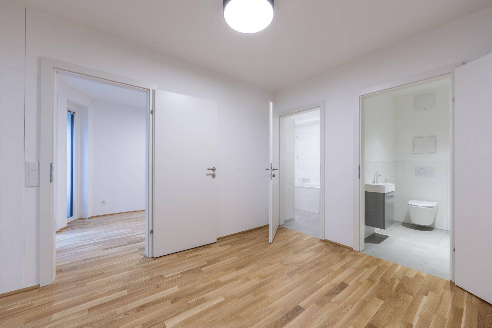 Geräumiges Zimmer mit Parkettboden und offenen Türen zu einem Badezimmer und einem weiteren Wohnbereich.
