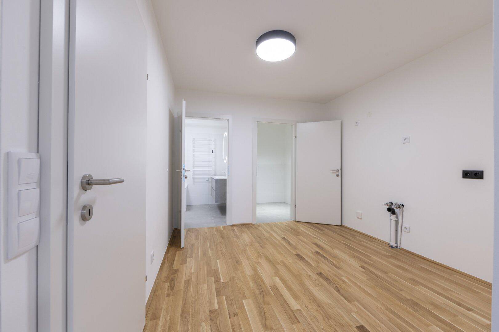 Heller Raum mit Parkettboden und Zugang zu einem modernen Badezimmer, ideal als Schlaf- oder Gästezimmer.