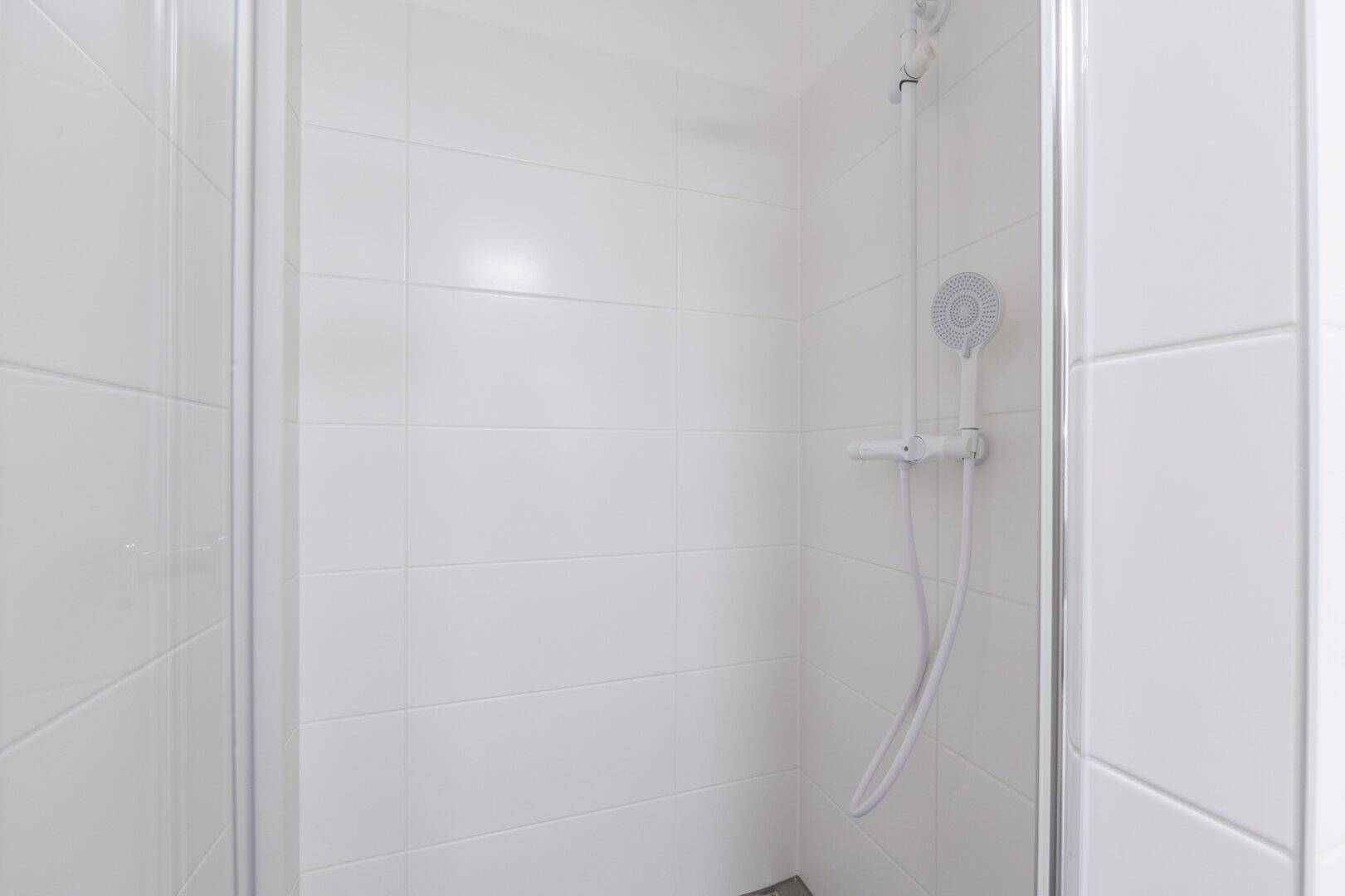 Moderne Duschkabine mit weißen Fliesen und einfacher Duscharmatur, sauber und funktional gestaltet.