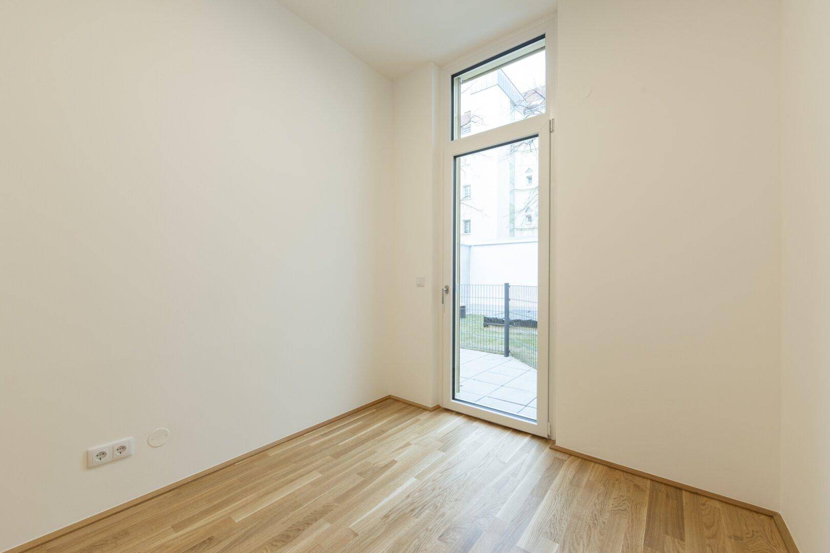 Helles Zimmer mit Parkettboden und bodentiefer Fenstertür, die direkten Zugang zum Außenbereich bietet.