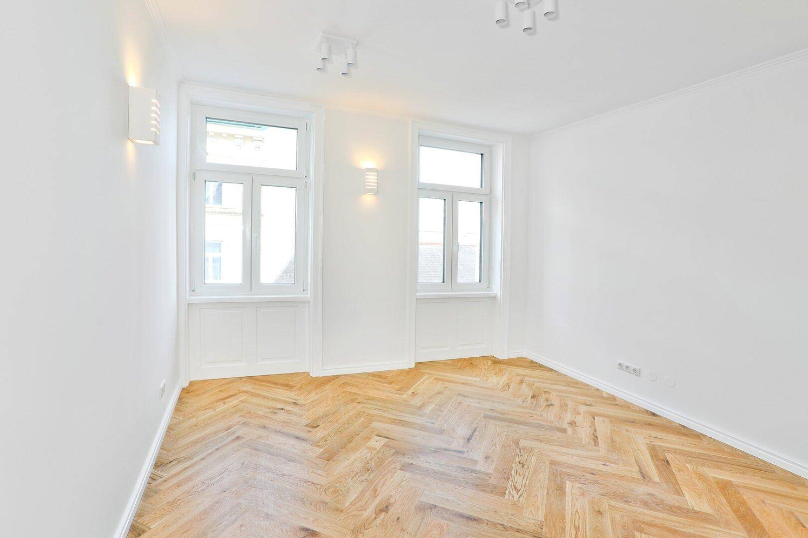 Lichtdurchflutetes Zimmer mit Fischgrätparkett und modernen Wandleuchten.
