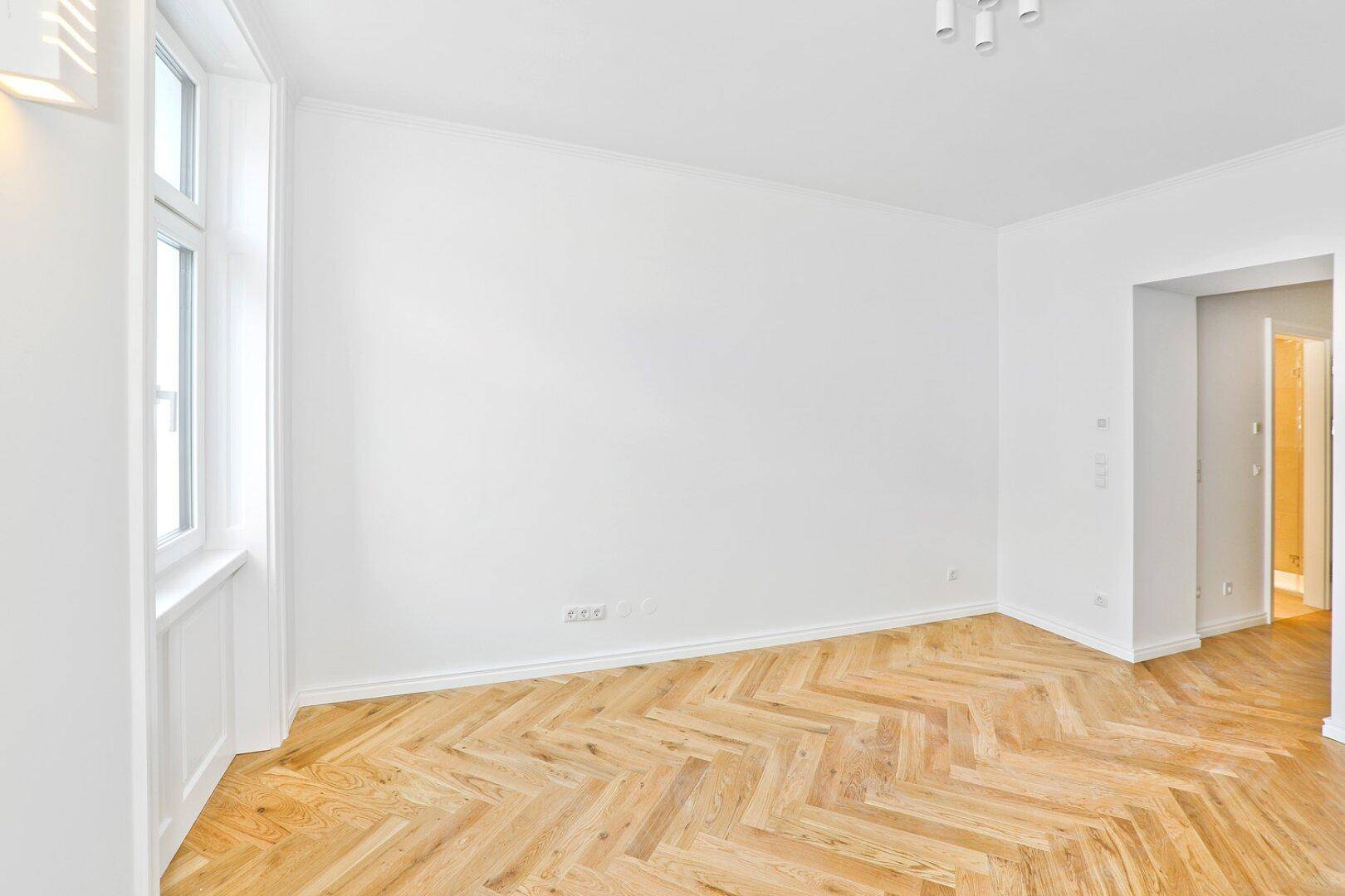 Geräumiges Zimmer mit Fischgrätparkett und Zugang zu weiteren Räumen.