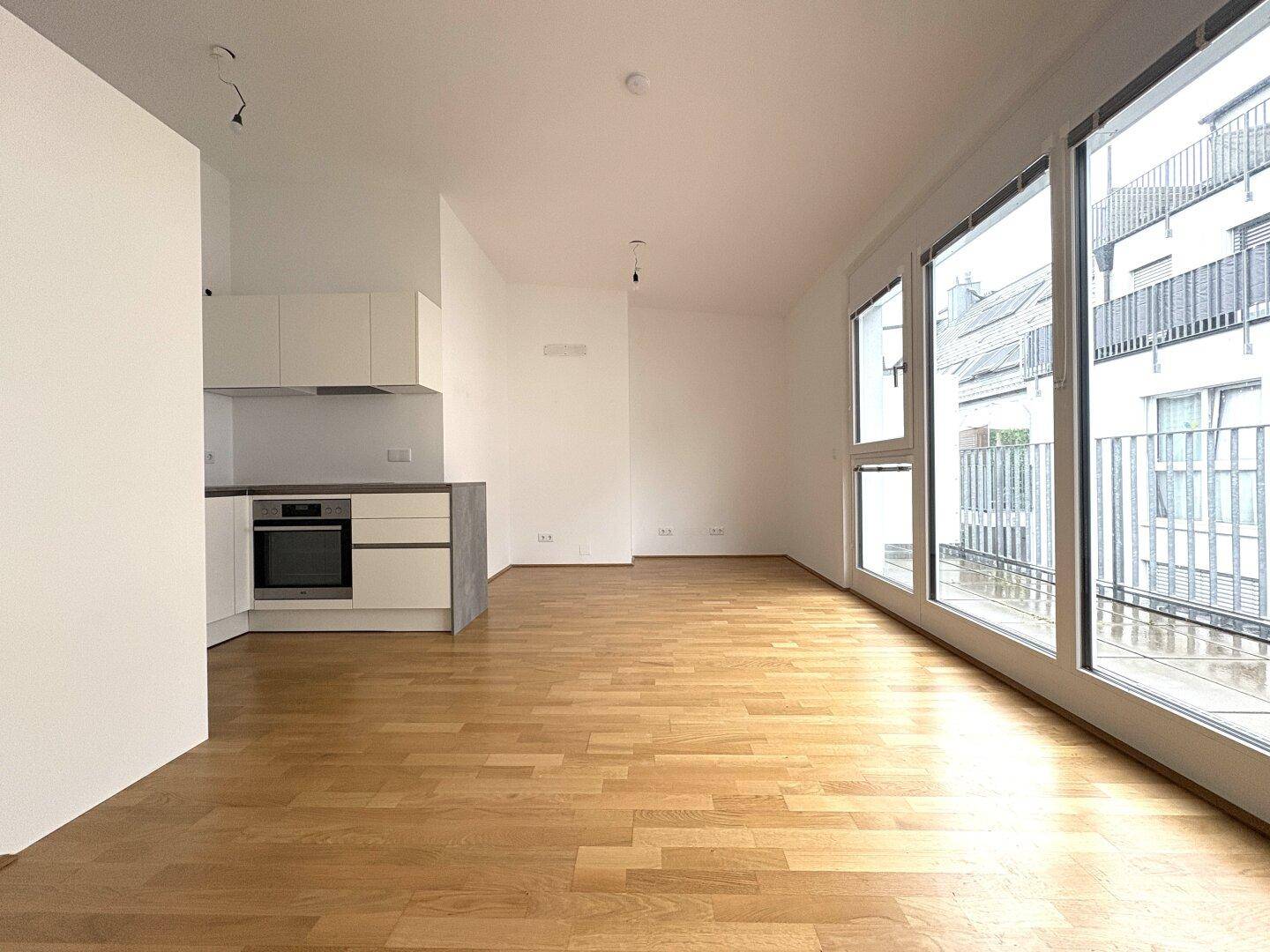 Geräumiger offener Wohnbereich mit moderner Küchenzeile und großen Fenstern zum Balkon.