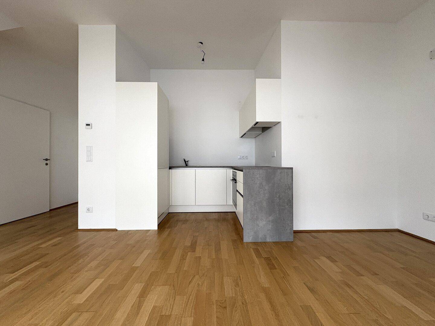 Moderne Einbauküche in Weiß mit grauer Arbeitsplatte und integrierten Geräten.