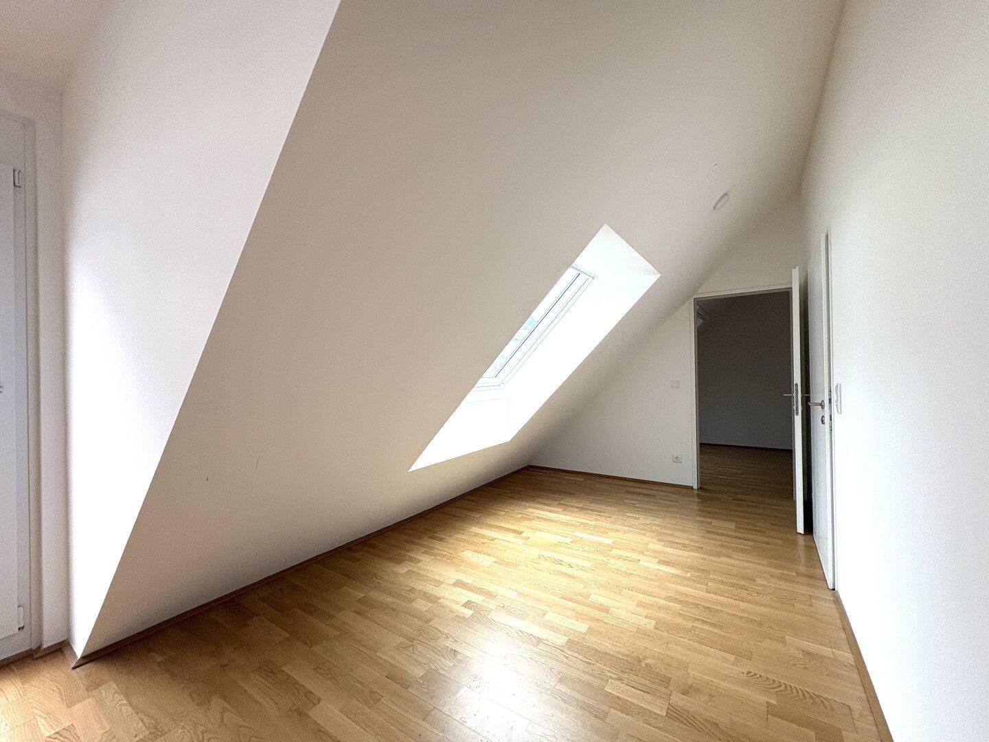 Geräumiges Dachzimmer mit Holzboden und schrägem Dachfenster, ideal als Schlafzimmer.