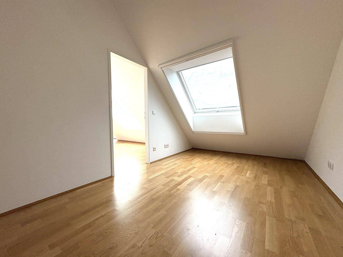 Helles Dachzimmer mit Parkettboden und großem Dachfenster, bietet viel Tageslicht.