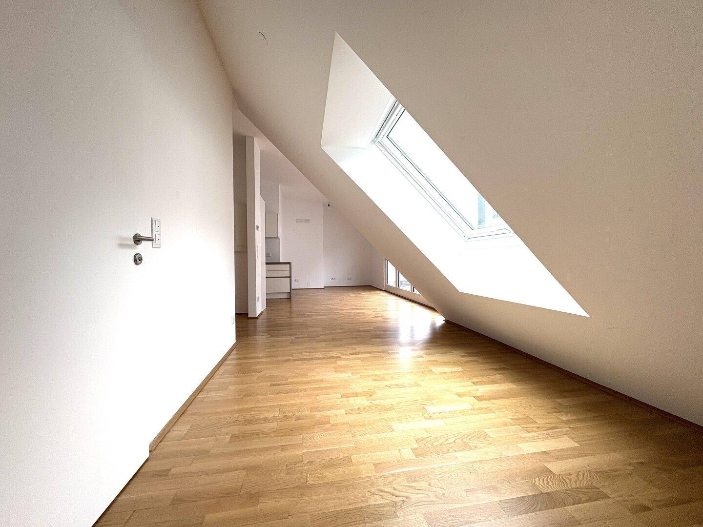 Lichtdurchflutetes Dachzimmer mit Holzboden und schrägem Dachfenster, offen zum Flur.