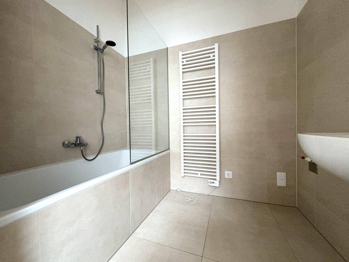 Modernes Badezimmer mit beigefarbenen Fliesen, Badewanne und beheiztem Handtuchhalter.