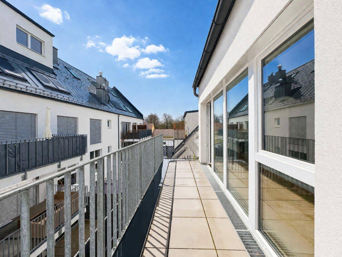 Langer Balkon mit Fliesenboden und Metallgeländer, bietet einen Blick auf die Nachbarschaft.