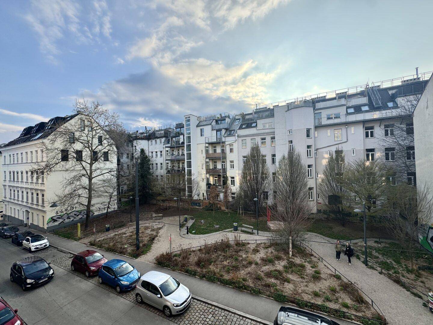 Blick auf eine Wohngegend mit mehreren Gebäuden, einer Straße und einer Grünfläche mit Bäumen.