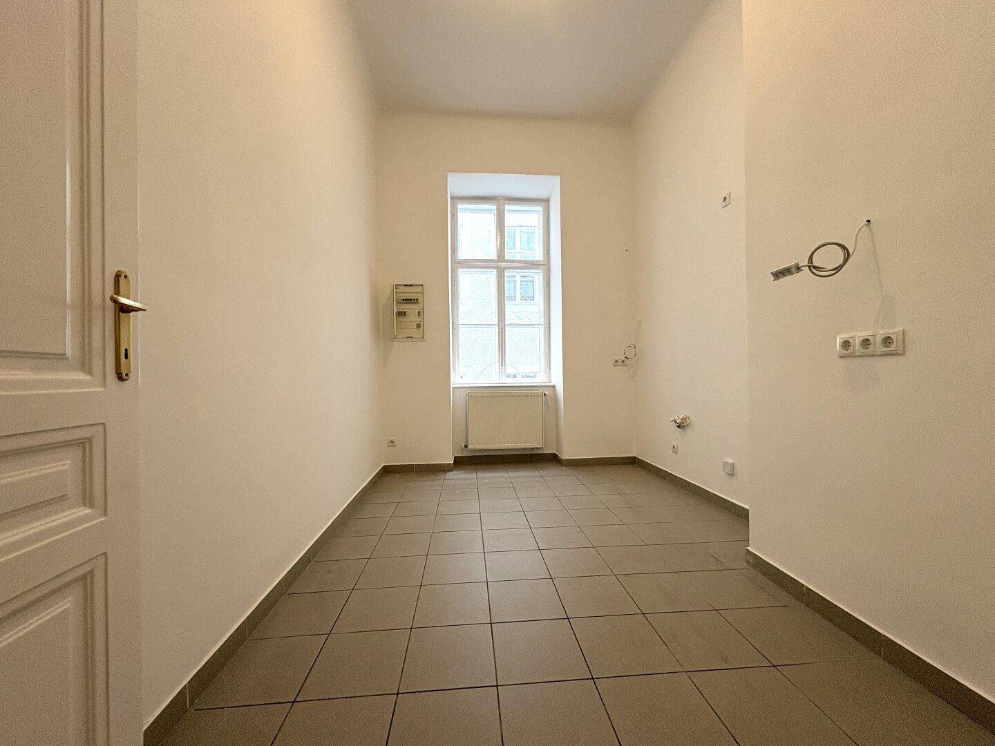 Leerer Küchenraum mit Fliesenboden und einem Fenster, bereit für die Installation einer Einbauküche.