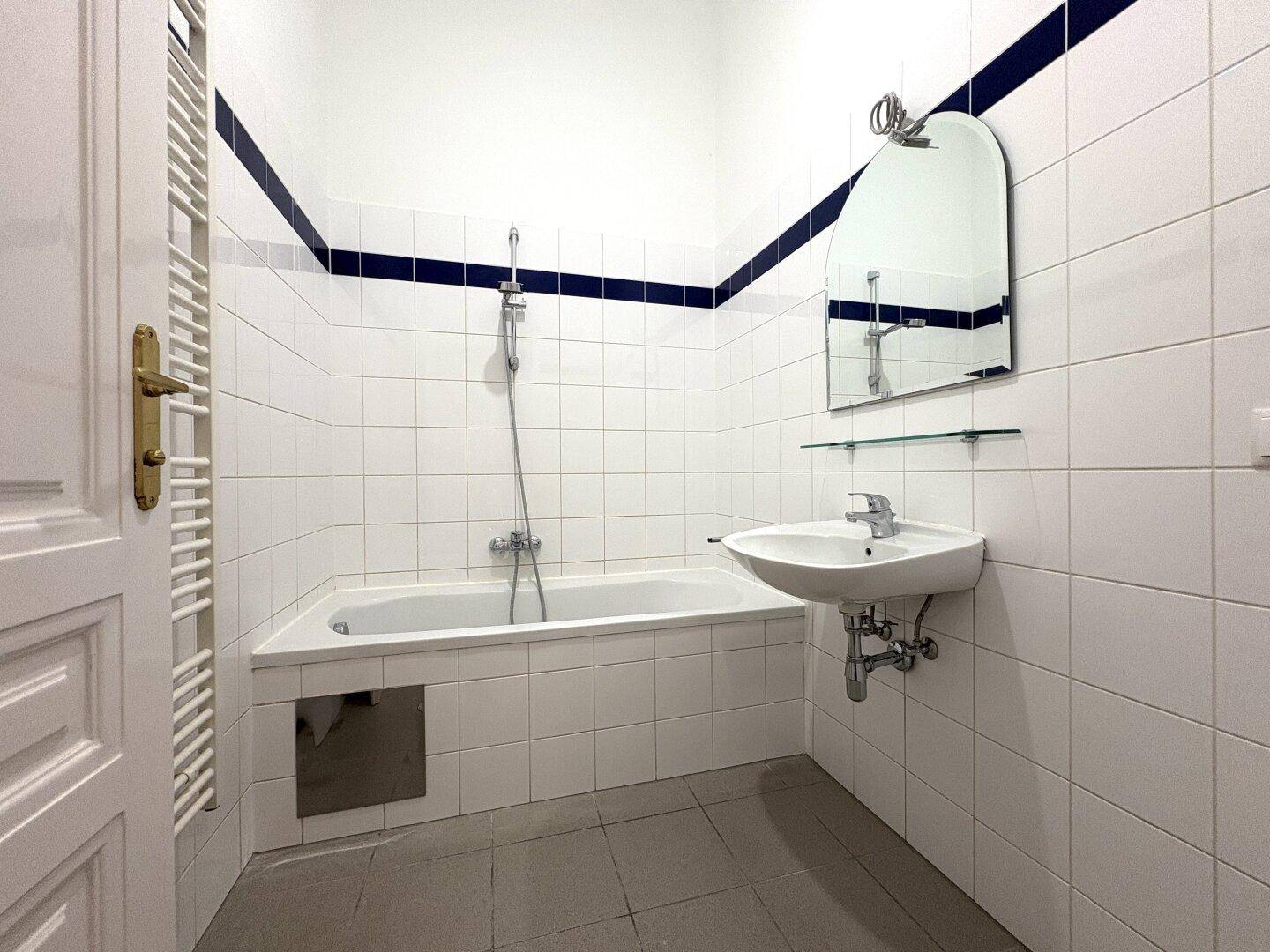 Badezimmer mit weiß gefliesten Wänden, Badewanne und einem beheizten Handtuchhalter.