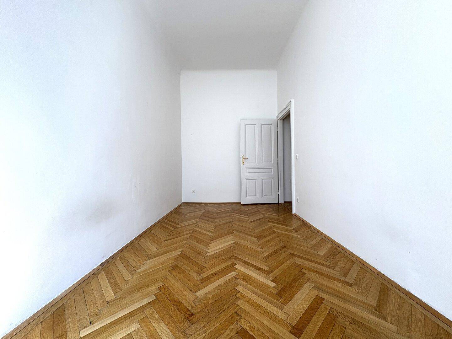 Leeres Zimmer mit Fischgrätparkettboden und einer weißen Tür, bereit zur individuellen Gestaltung.