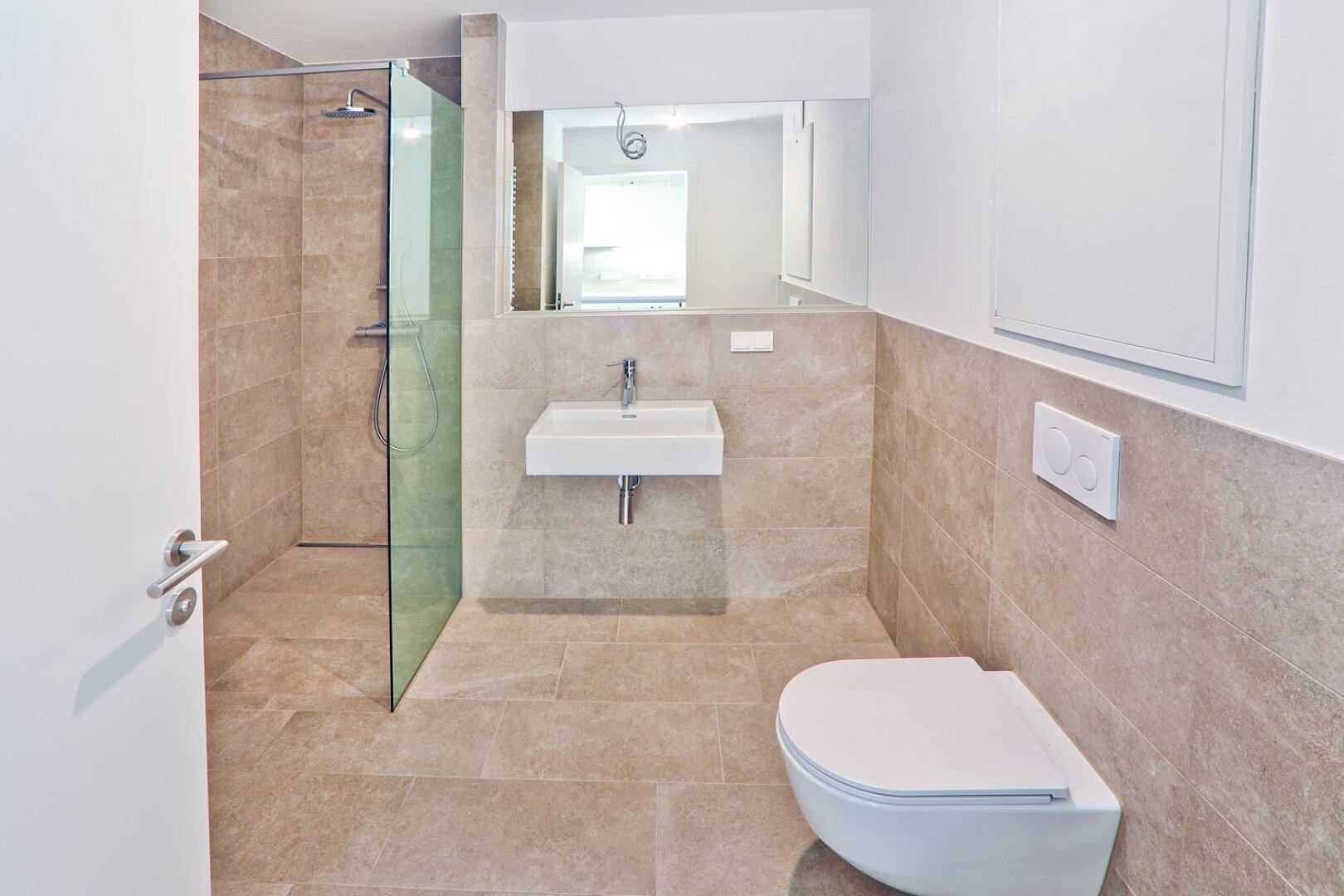 Modernes Badezimmer mit beigefarbenen Fliesen, ebenerdiger Dusche und wandhängendem WC.