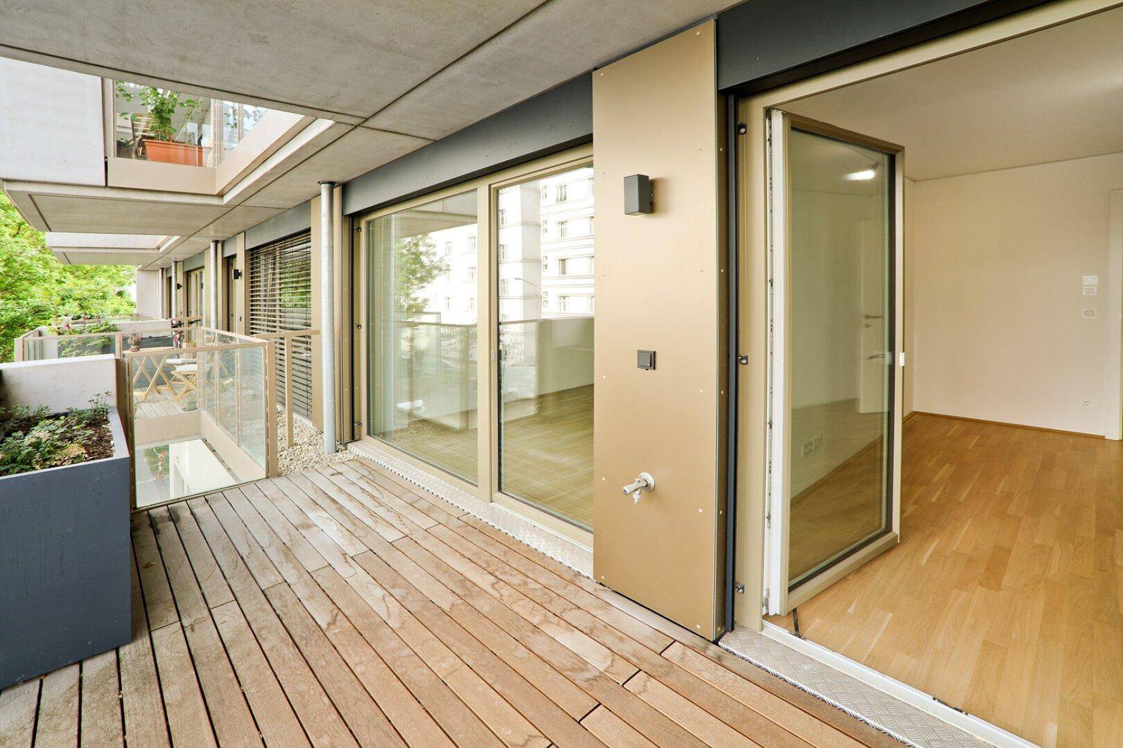 Geräumiger Balkon mit Holzfußboden und Zugang vom Innenbereich der Wohnung.