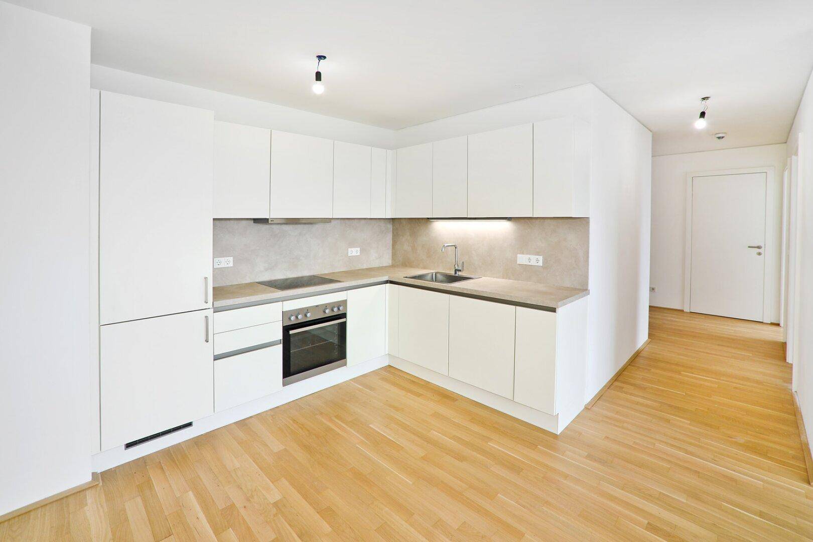 Moderne Einbauküche in Weiß mit integrierten Geräten und hellem Parkettboden.