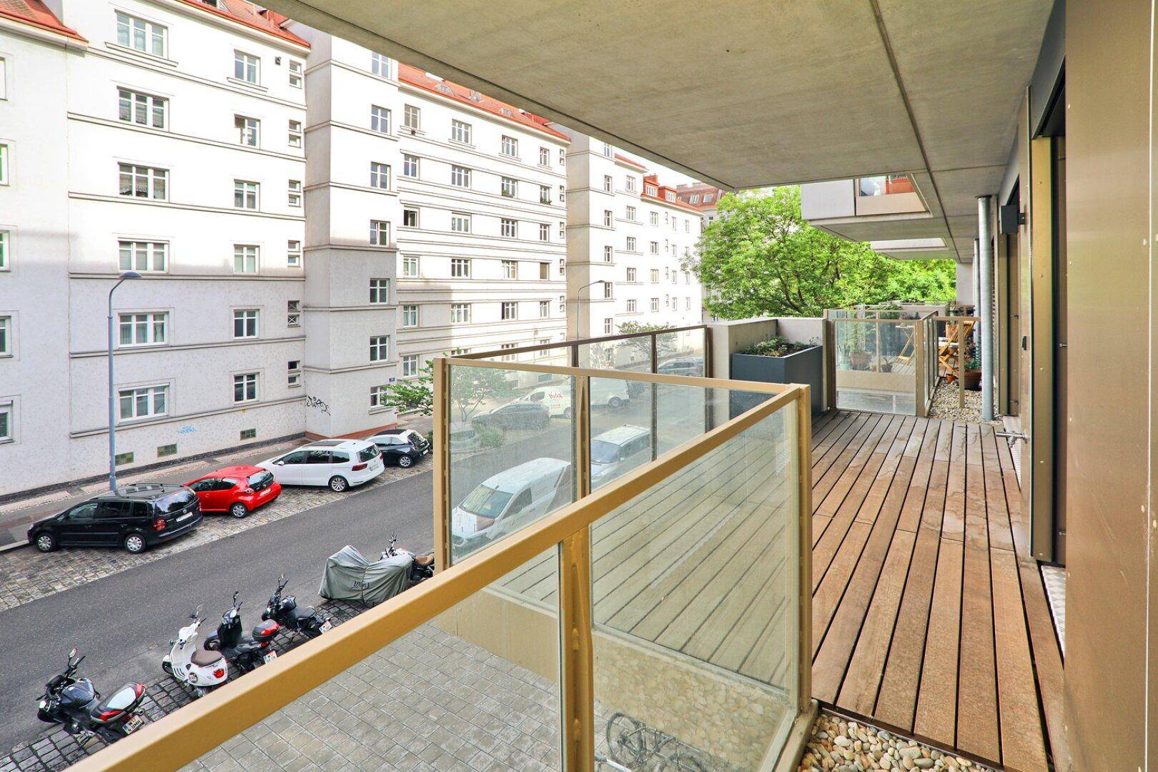 Geräumiger Balkon mit Holzbelag und Blick auf die Straße und umliegende Gebäude.